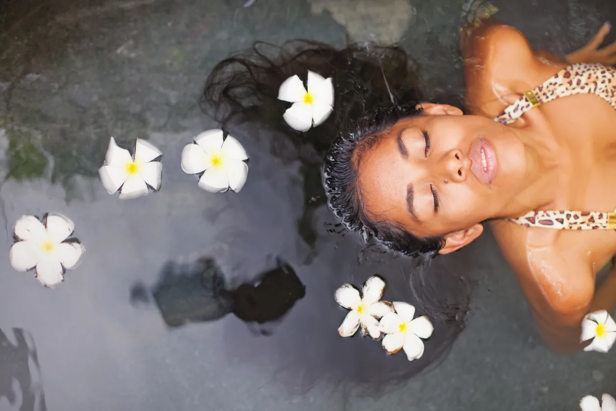Exotic woman enjoying bath ritual with frangipani flowers